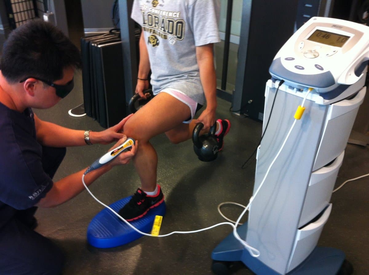 A KOH Physical Therapy Lab therapist using a handheld cold laser on an athlete's knee on the clinic training floor
