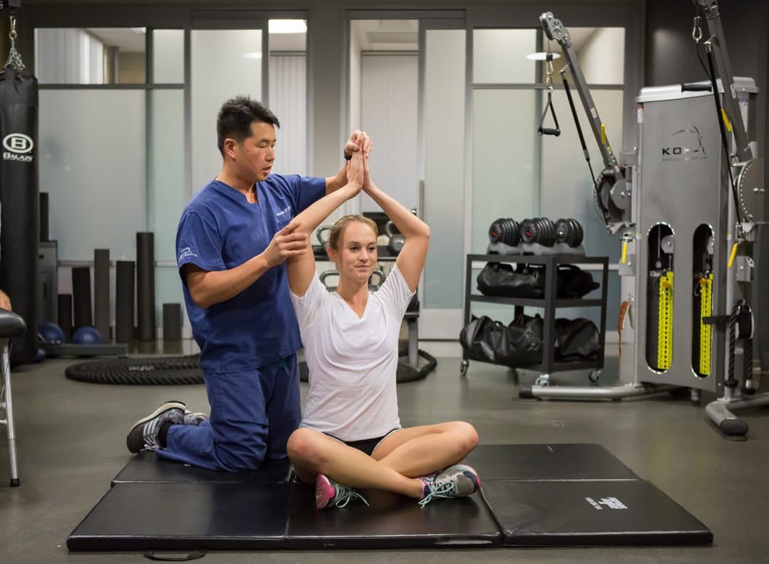 Davis Koh, DPT, guiding a client through an assisted overhead fascia stretch on the training floor