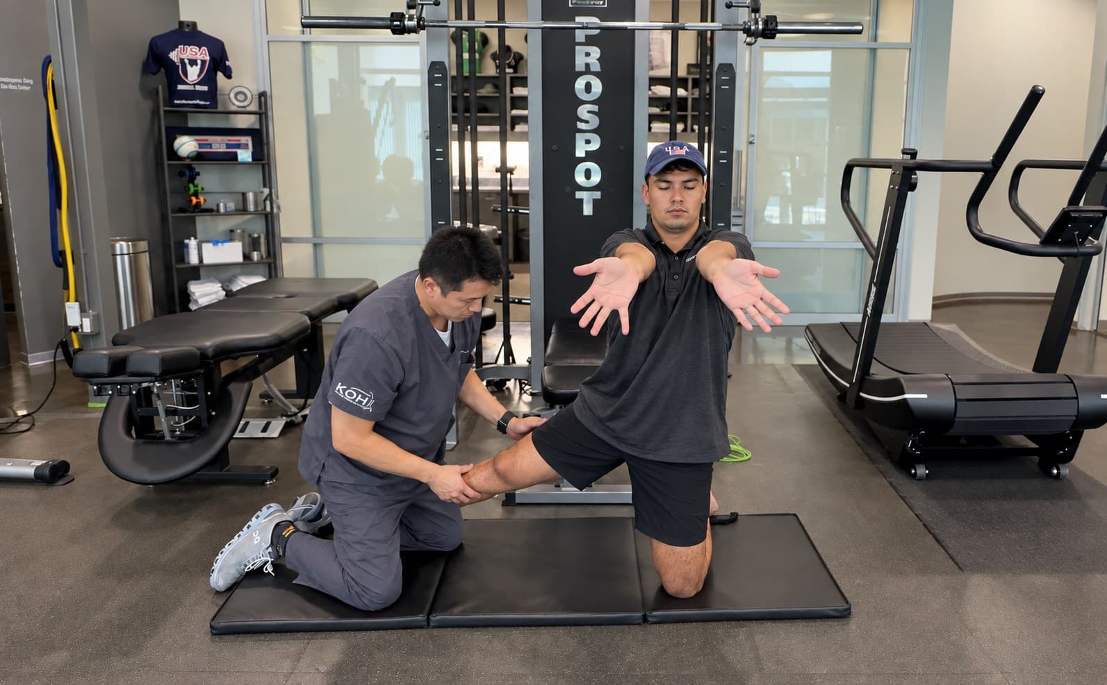 A KOH Physical Therapy Lab therapist assisting a kneeling patient with an arm and trunk fascia stretch