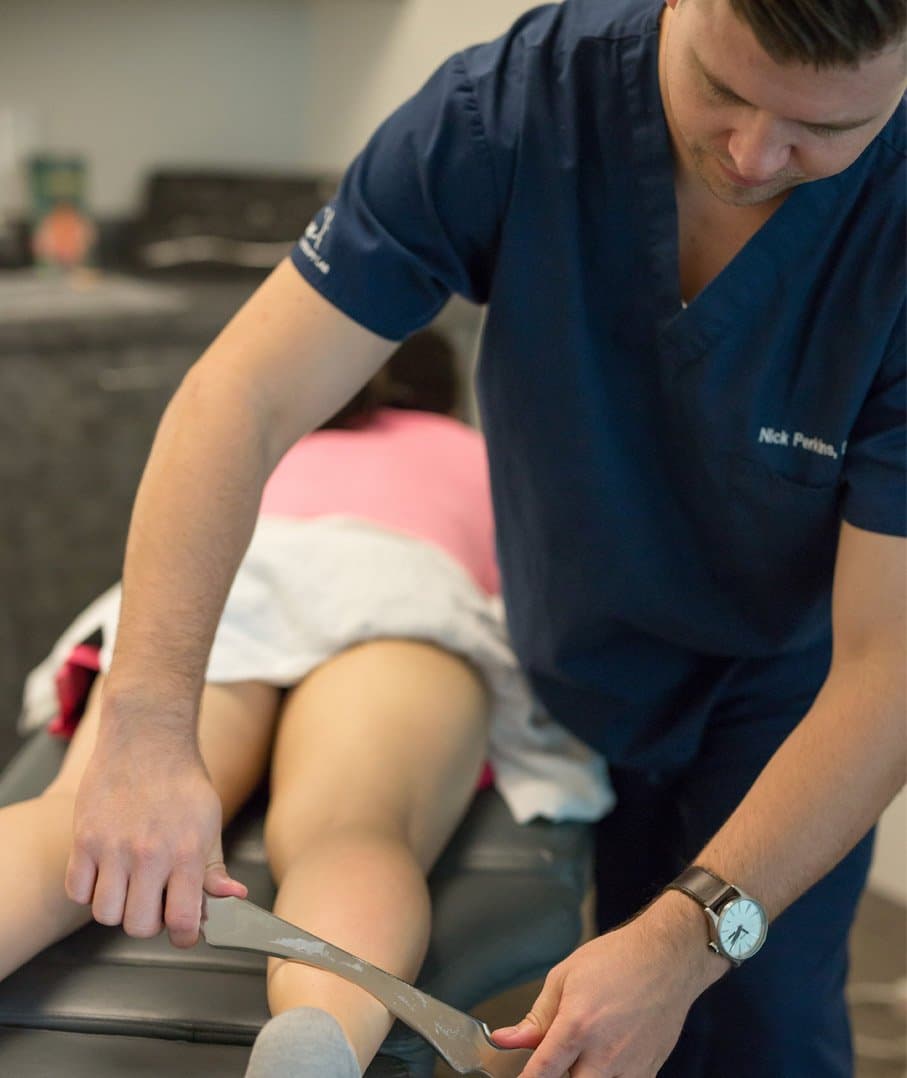 A KOH Physical Therapy Lab physical therapist using a stainless steel soft tissue instrument on the back of a client's thigh