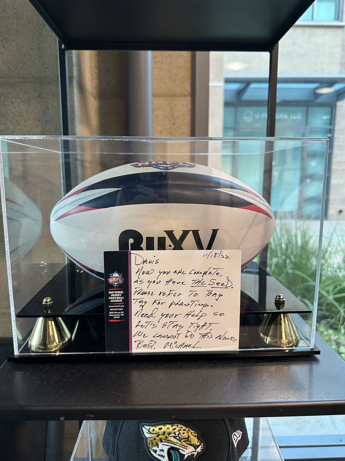 A rugby ball in a display case with a handwritten note to Davis, on a shelf at the KOH Physical Therapy Lab clinic