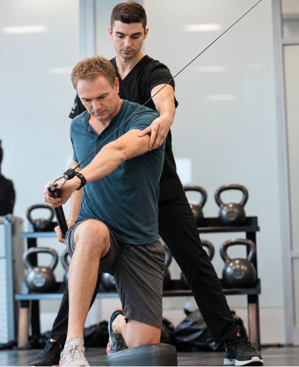 A KOH Physical Therapy Lab physical therapist guiding a client's arm and trunk position during a half-kneeling cable rotation exercise