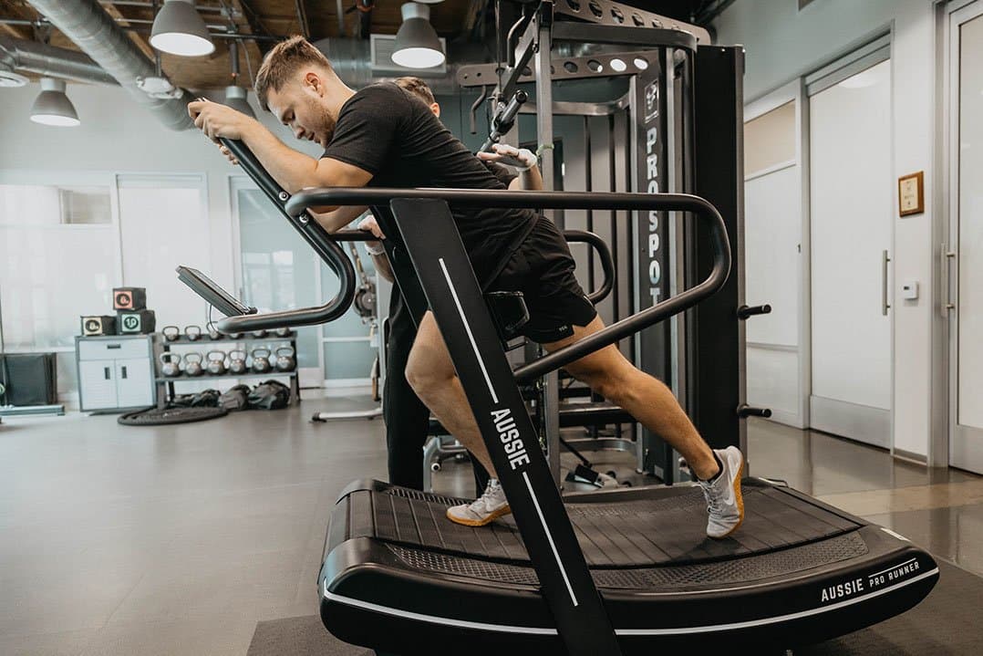 A client training on a curved manual treadmill with a physical therapist spotting him on the KOH Physical Therapy Lab training floor