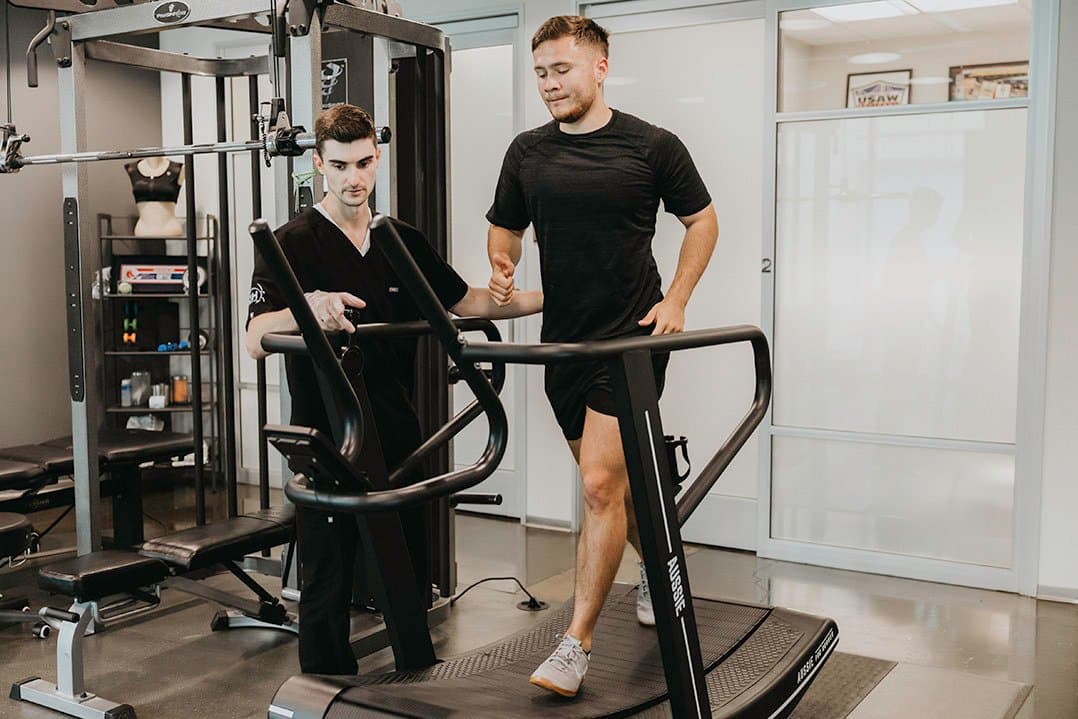 A KOH Physical Therapy Lab physical therapist coaching a client on a curved manual treadmill on the clinic training floor