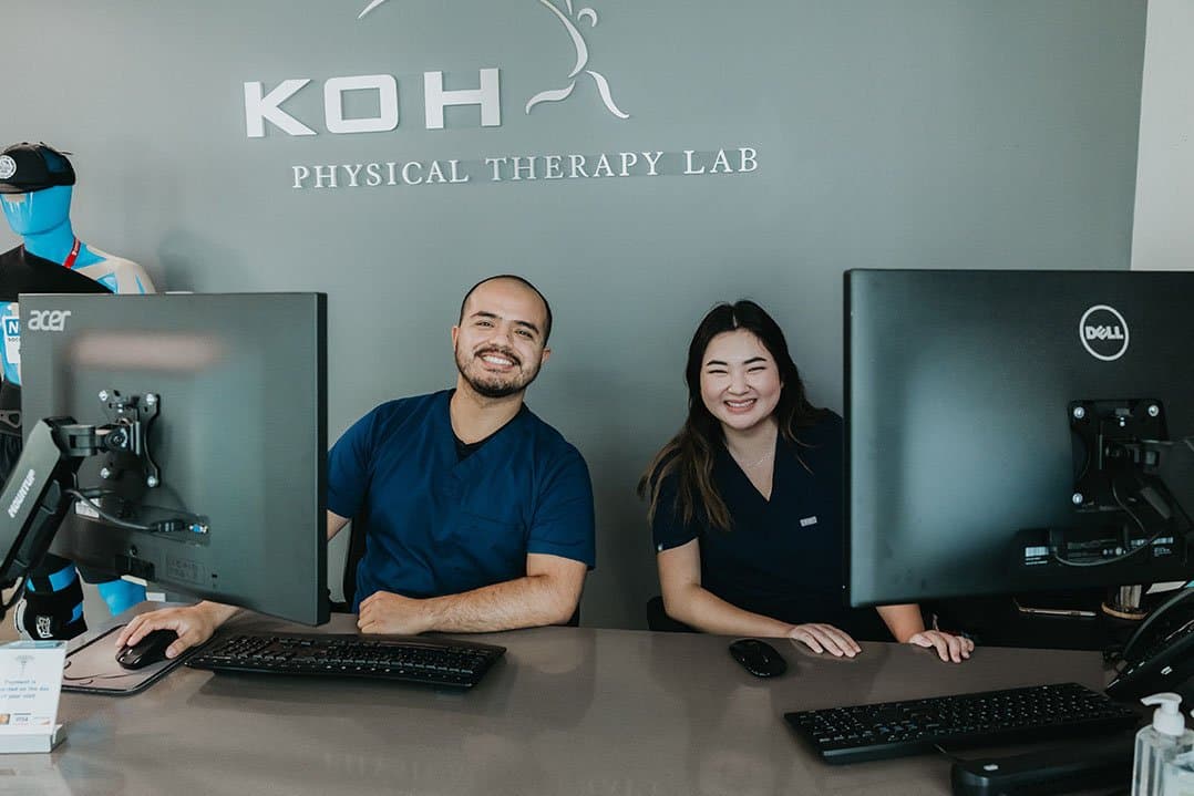 Two team members at the front desk beneath the KOH Physical Therapy Lab sign