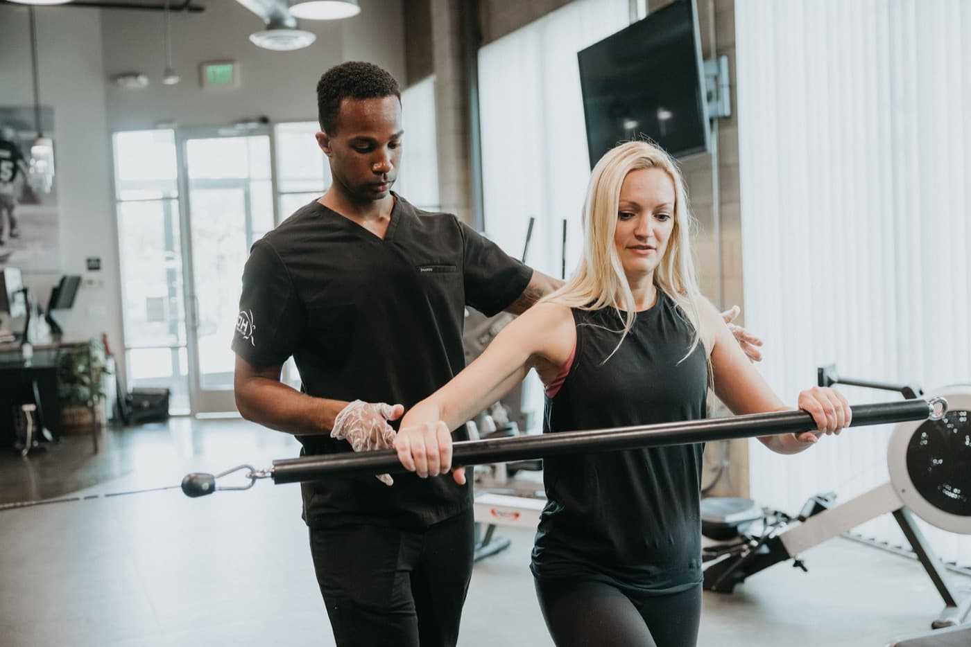 A KOH Physical Therapy Lab therapist guiding a patient through a cable bar exercise for shoulder and trunk control