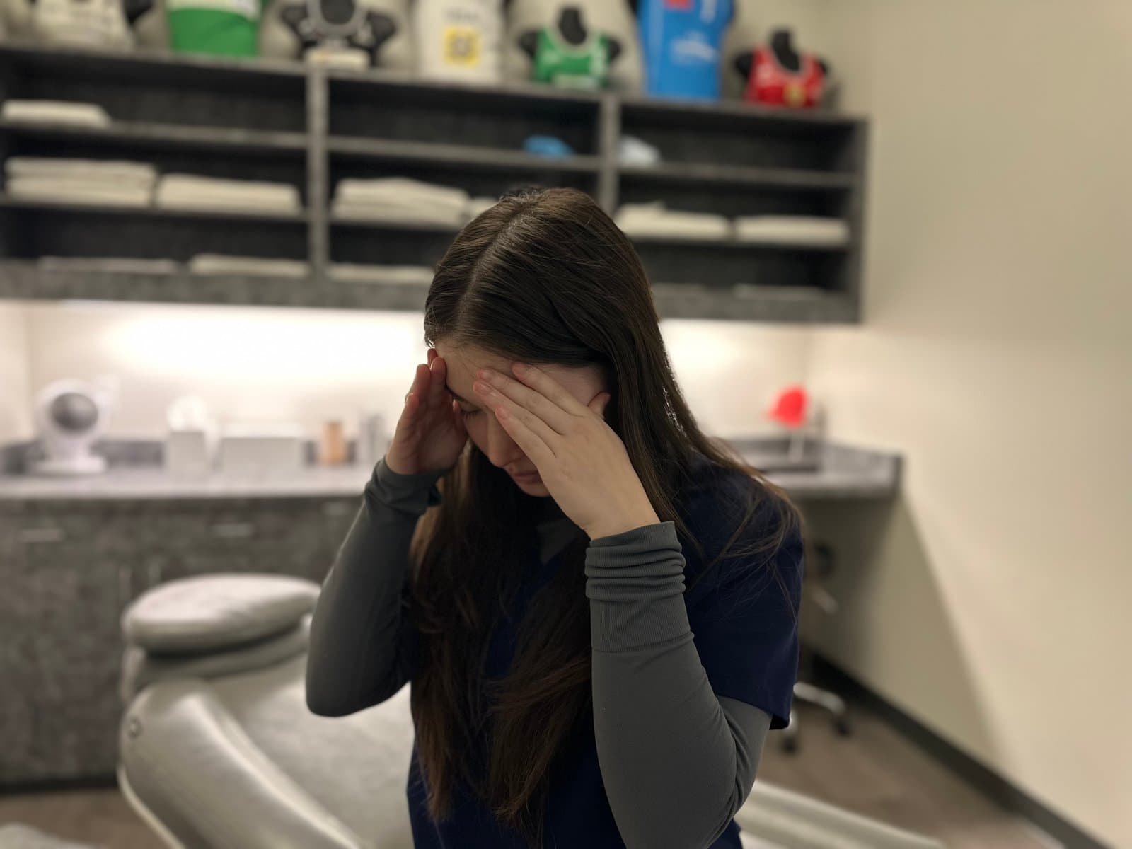 A person holding her head with both hands, feeling dizzy, in a KOH Physical Therapy Lab treatment room
