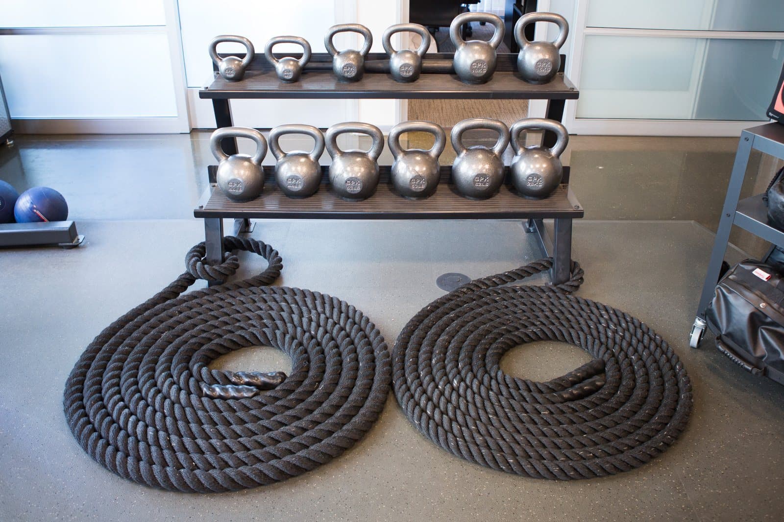Two coiled battling ropes on the floor in front of a rack of kettlebells at KOH Physical Therapy Lab