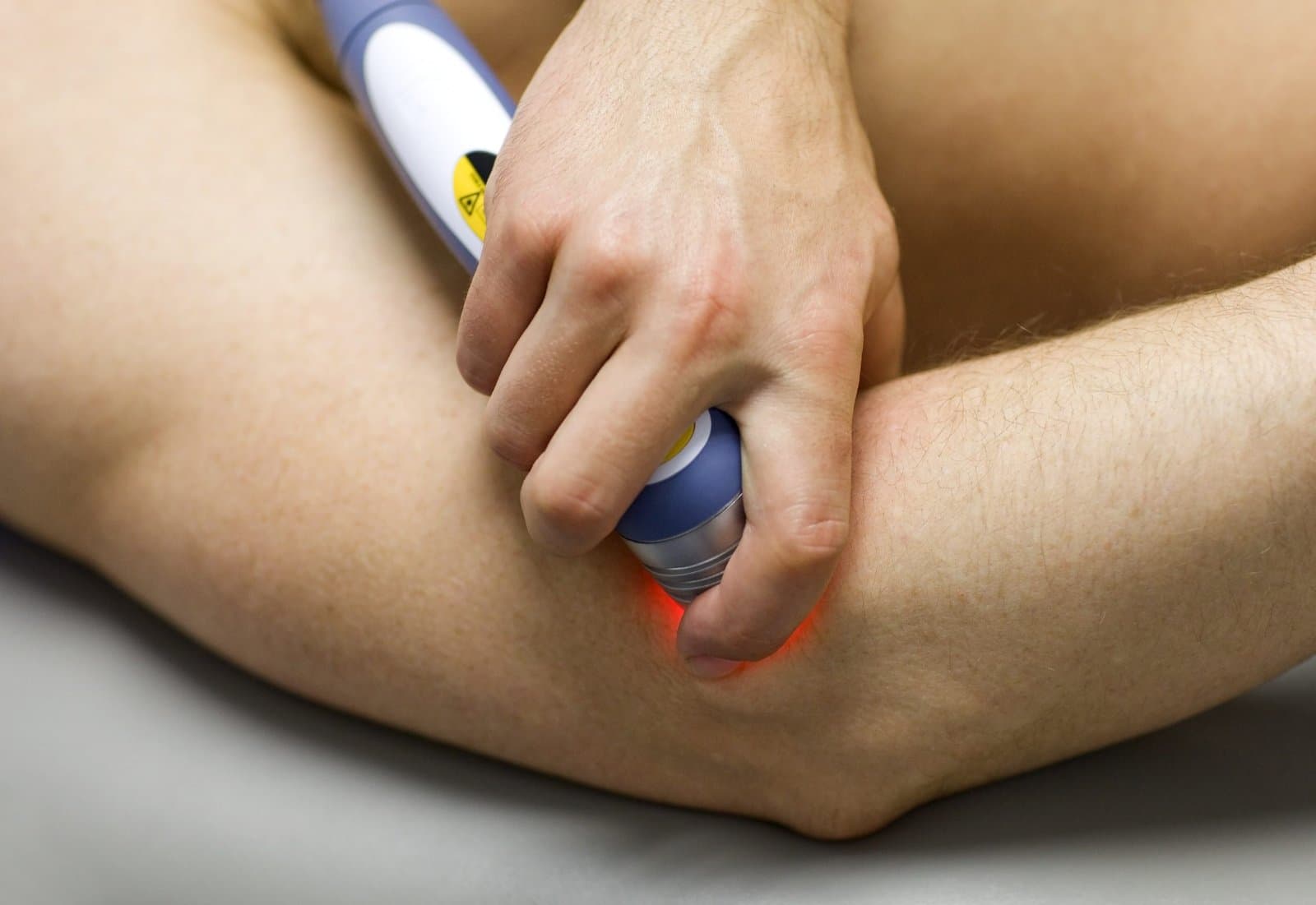 A handheld cold laser probe glowing red against the outside of a client's elbow