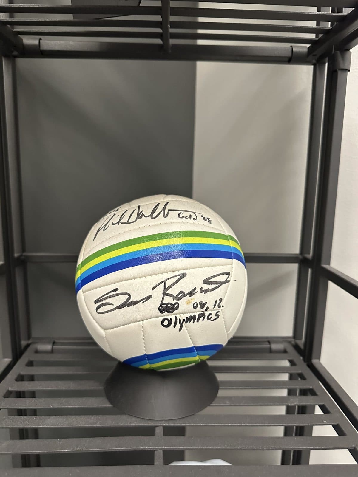 A signed beach volleyball marked 08 and 12 Olympics on a display stand