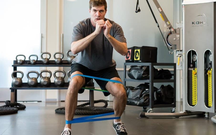 A patient doing a squat with resistance bands around his knees and ankles on the KOH Physical Therapy Lab training floor