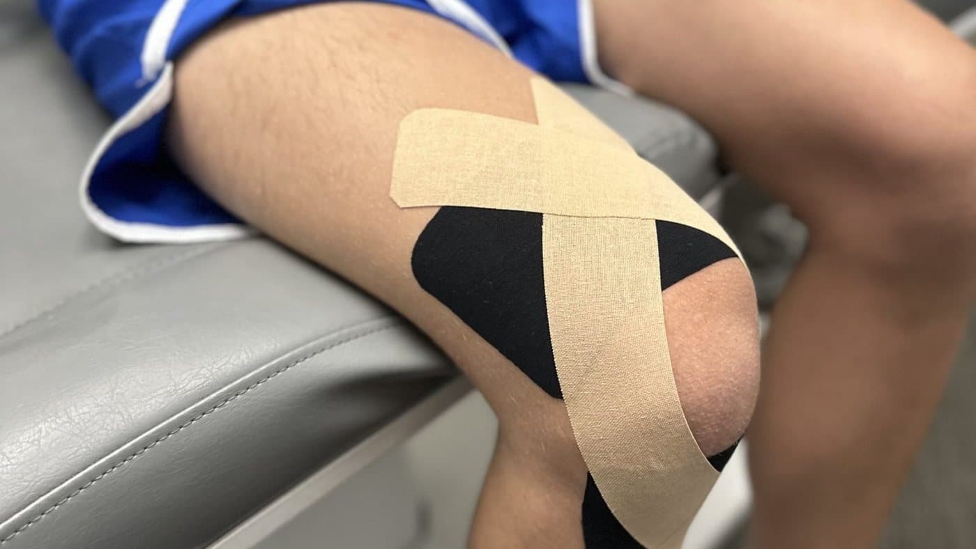 Beige and black kinesiology tape applied in a crossing pattern around a client's knee