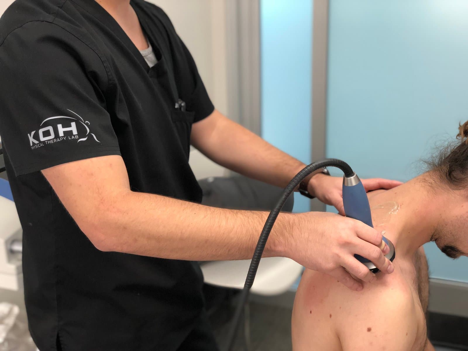 A KOH Physical Therapy Lab therapist applying focused shockwave therapy to a client's upper shoulder with a handheld applicator