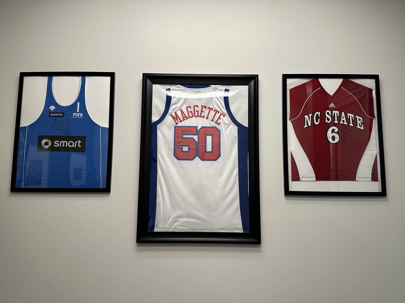 Three framed, signed athlete jerseys on a wall at KOH Physical Therapy Lab, with a Maggette number 50 jersey in the center