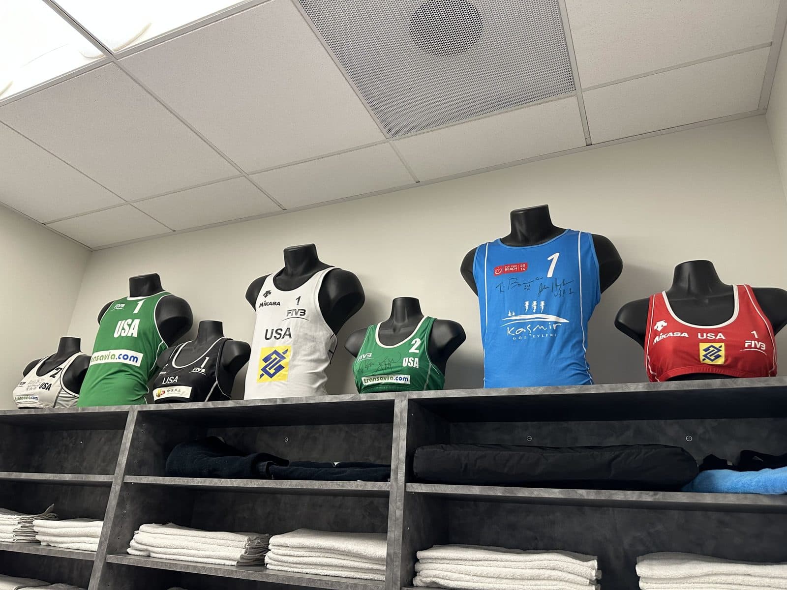 Team USA and international beach volleyball competition tops displayed on a shelf in a KOH Physical Therapy Lab treatment room